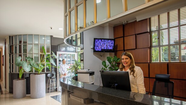Un mostrador de recepción con computadora, plantas en macetas y una pantalla de televisión.