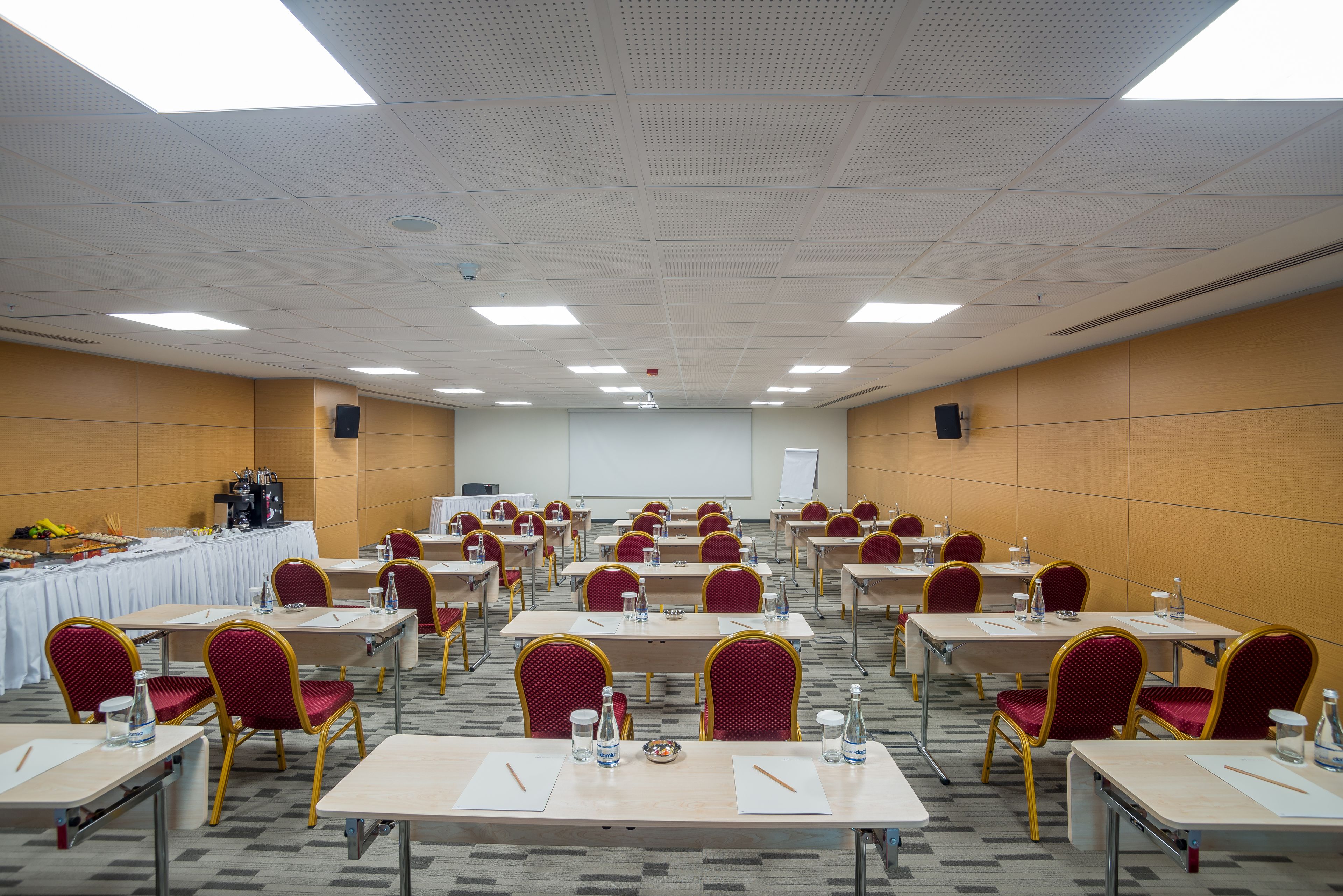A conference room with multiple tables and chairs, equipped with water bottles and notepads.