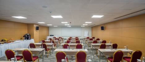 A conference room with multiple tables and chairs, equipped with water bottles and notepads.