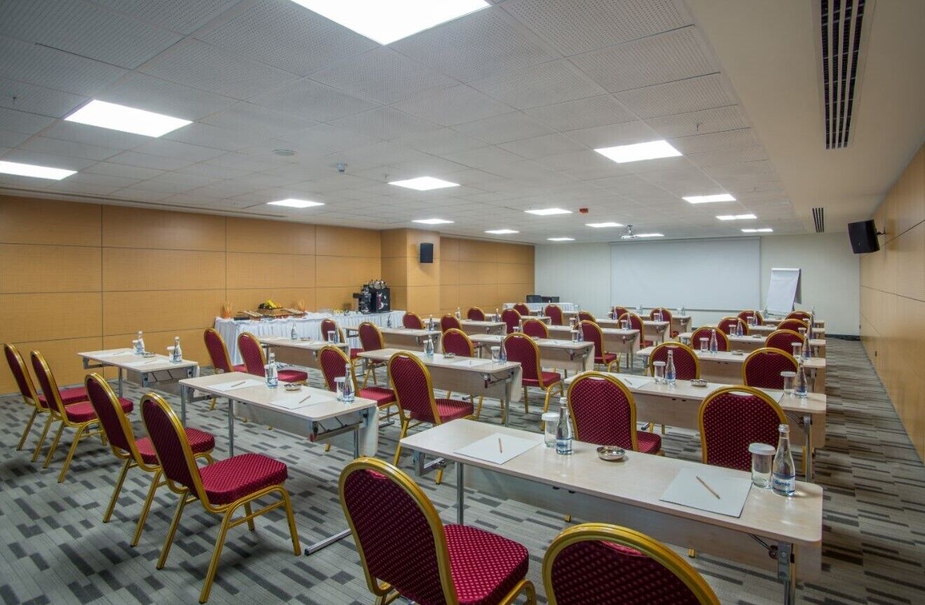 A conference room with rows of tables and chairs, equipped with water bottles and notepads.