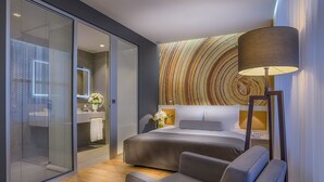 Habitación de hotel moderna con una cama grande, un sofá, una lámpara de pie y un amplio ventanal con vistas.