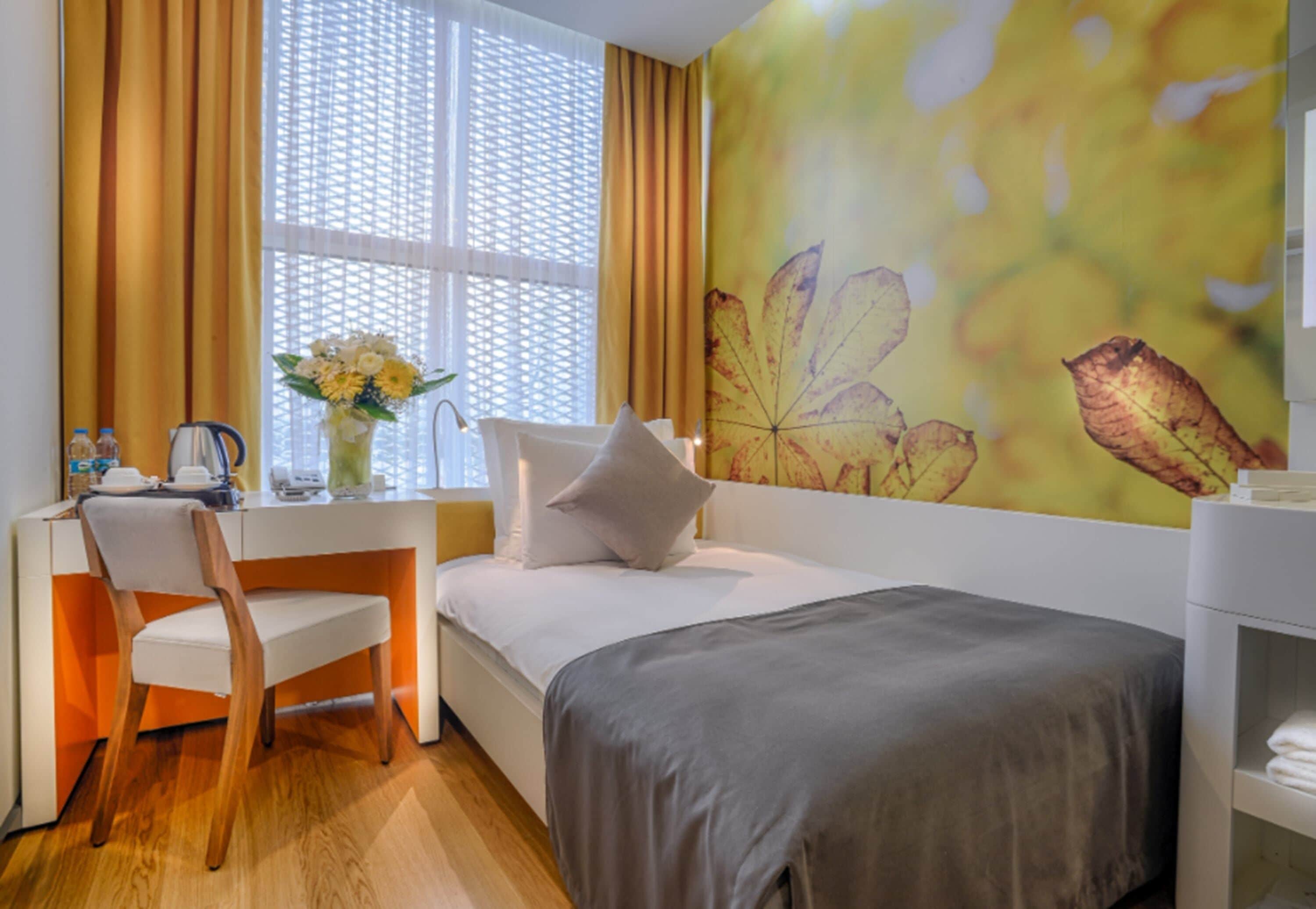 A bedroom with a bed, a desk, a chair, a vase with flowers, and a window with curtains.