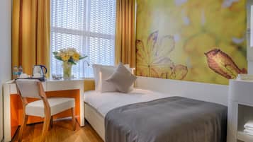 A bedroom with a bed, a desk, a chair, a vase with flowers, and a window with curtains.