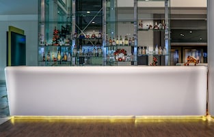 Zona de bar moderna con mostrador blanco y estantes llenos de botellas de licores.
