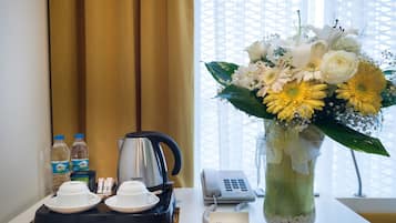 Una camera d'hotel con macchina del caffè, set per tè, telefono e un vaso di fiori sul tavolo.