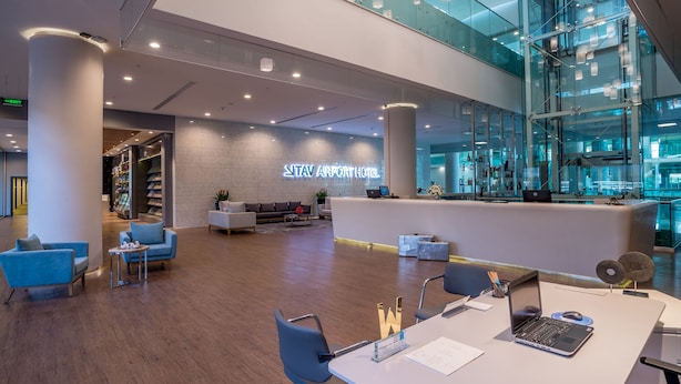 Un moderno vestíbulo de hotel con mostrador de recepción, zona de estar y un atrio de cristal.
