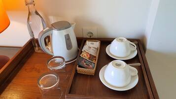 Una bandeja con un hervidor, dos tazas, una caja de café y un vaso.