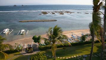 A beach view with boats, a palm tree, and a rocky breakwater.