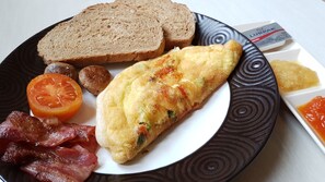 A plate with toast, bacon, a fried egg, a tomato slice, and a packet of butter. - Hotel Genggong (Karangasem)