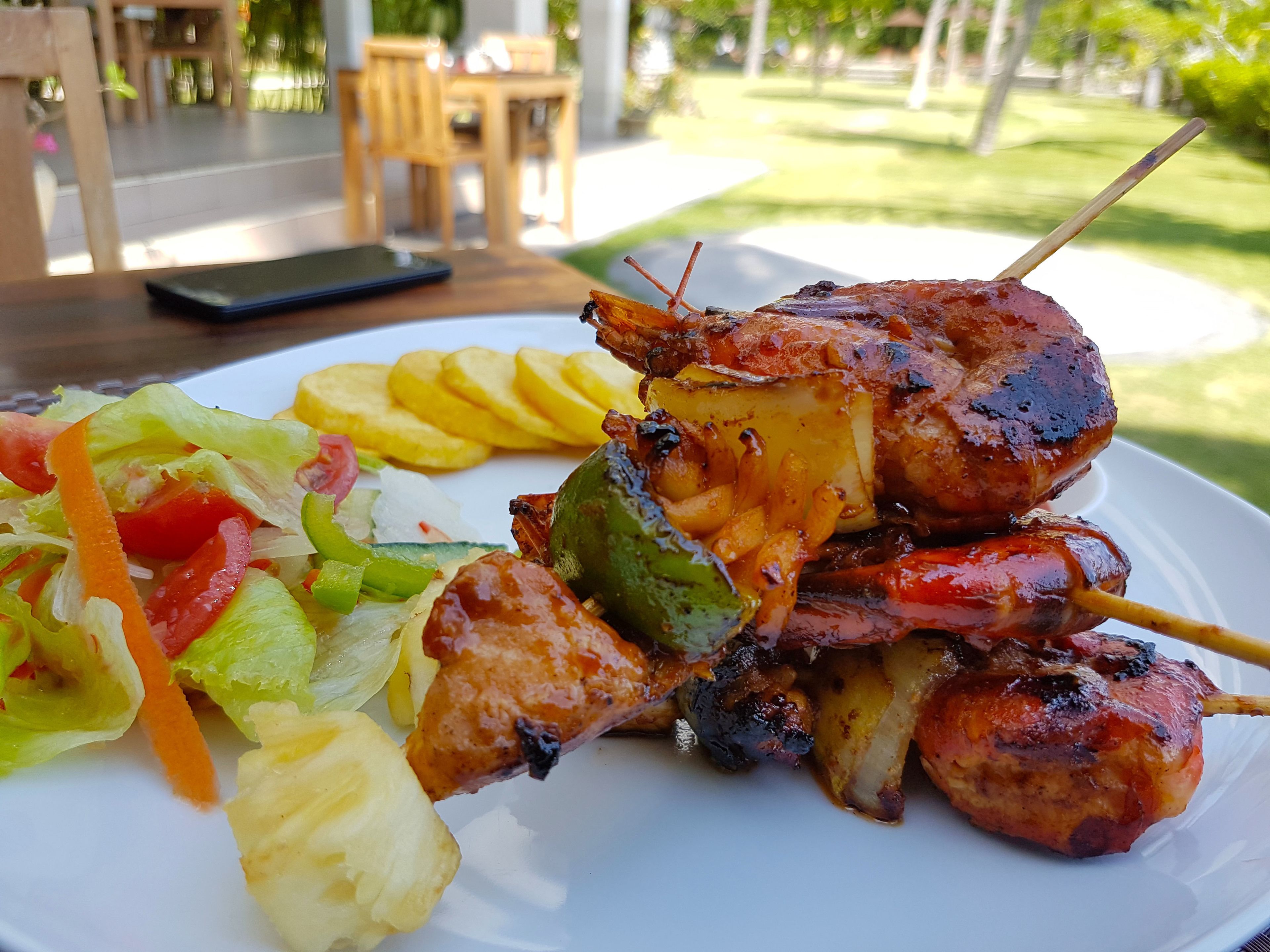 A plate of grilled meat skewers with vegetables and fries.