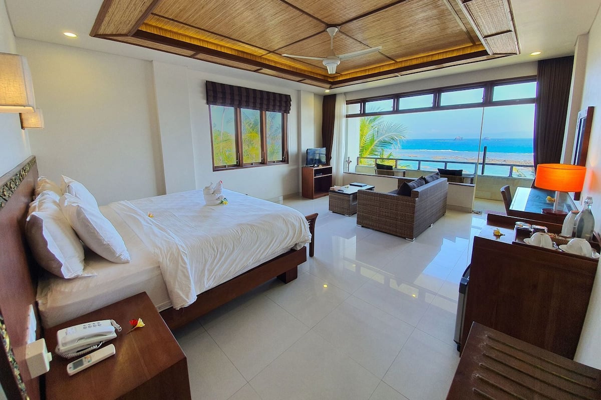 A hotel room with a bed, a sofa, a TV, a desk, and a view of the ocean.