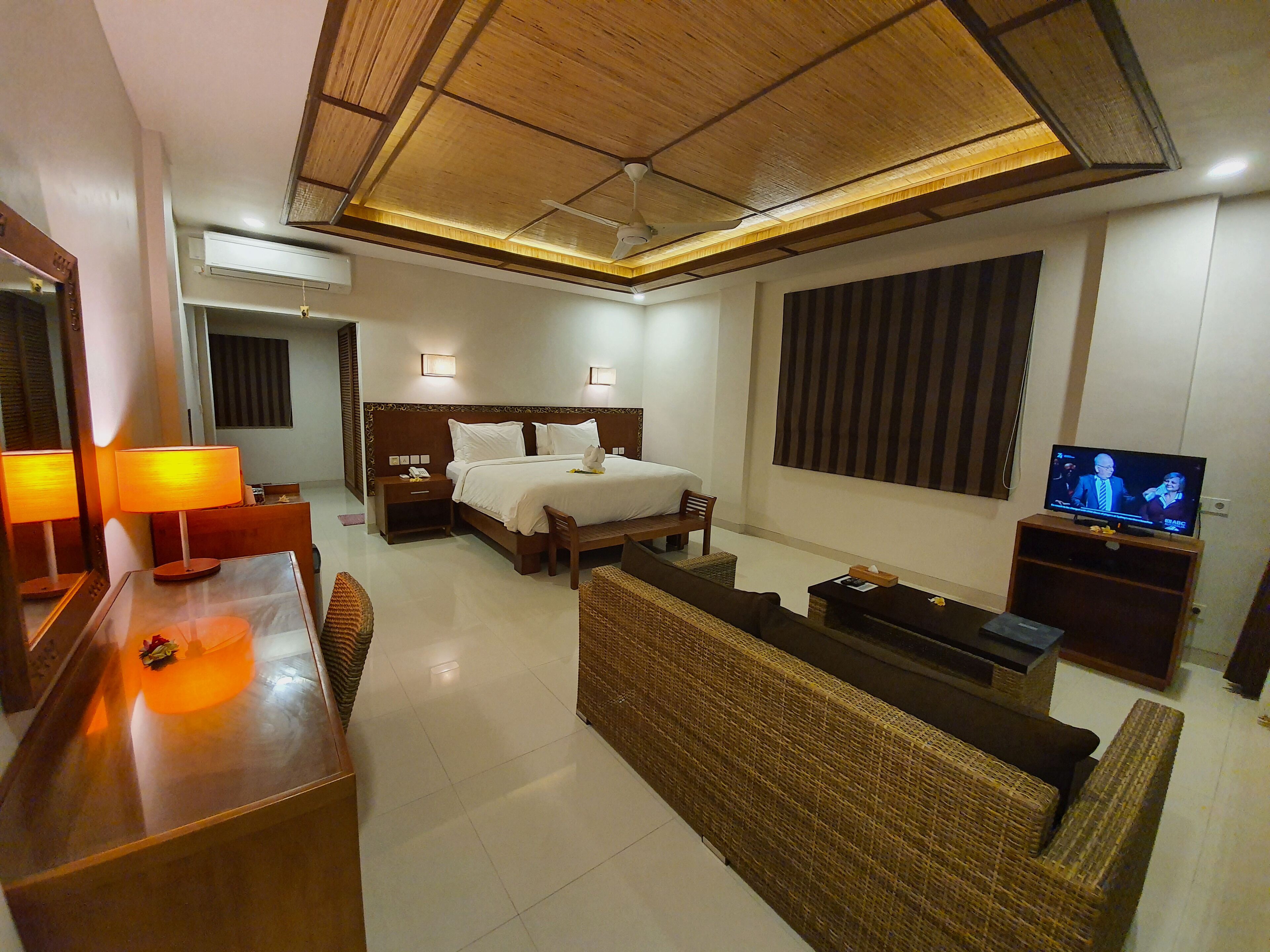 Habitación de hotel con cama, escritorio, televisor y sofá de mimbre.