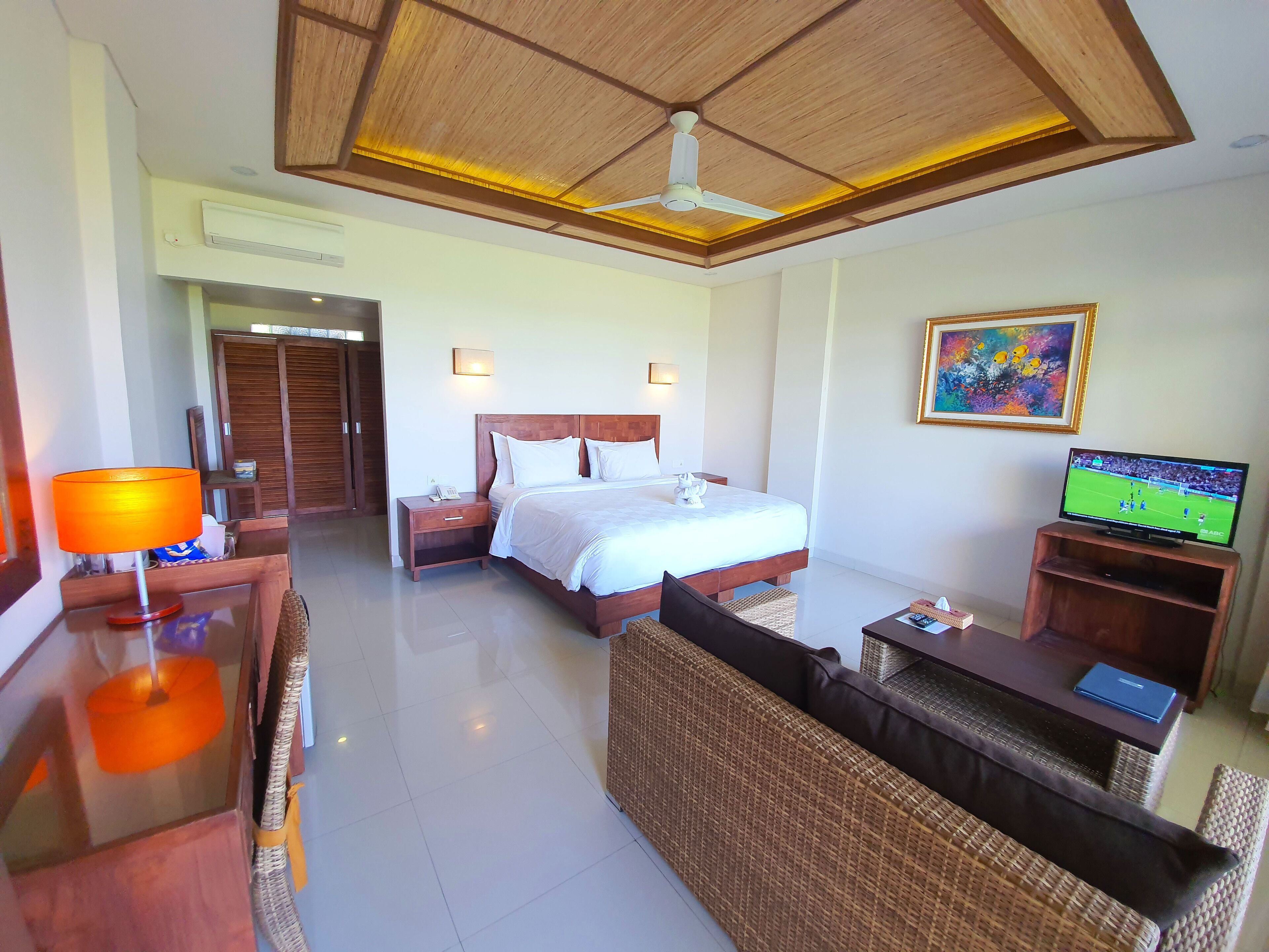 Una habitación de hotel con cama, escritorio, silla, televisor y ventilador de techo.