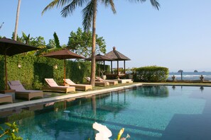 A pool area with lounge chairs and umbrellas, surrounded by greenery and overlooking the ocean. - Hotel Genggong (Karangasem)