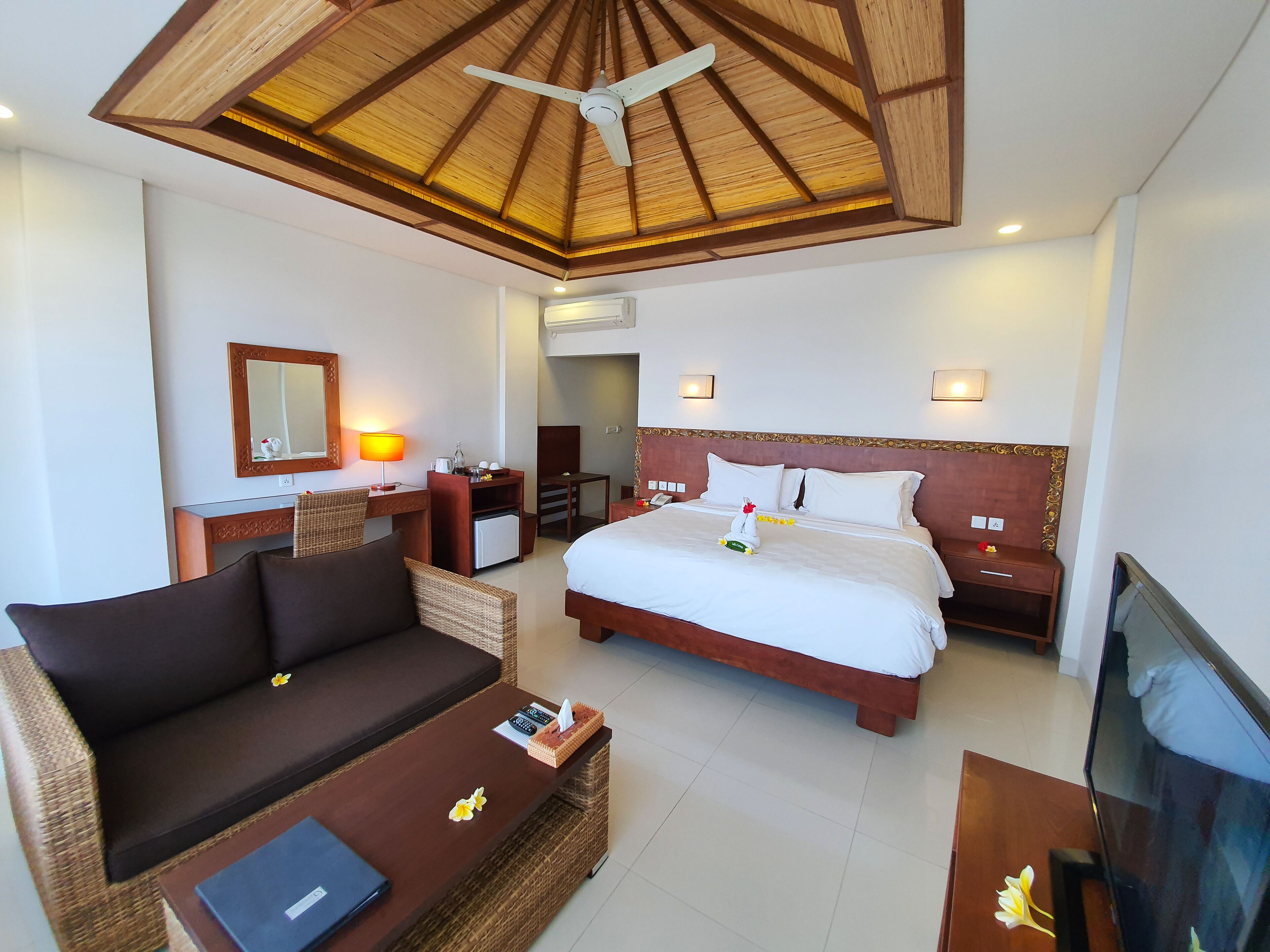 A hotel room with a bed, a sofa, a desk, a television, and a ceiling fan.
