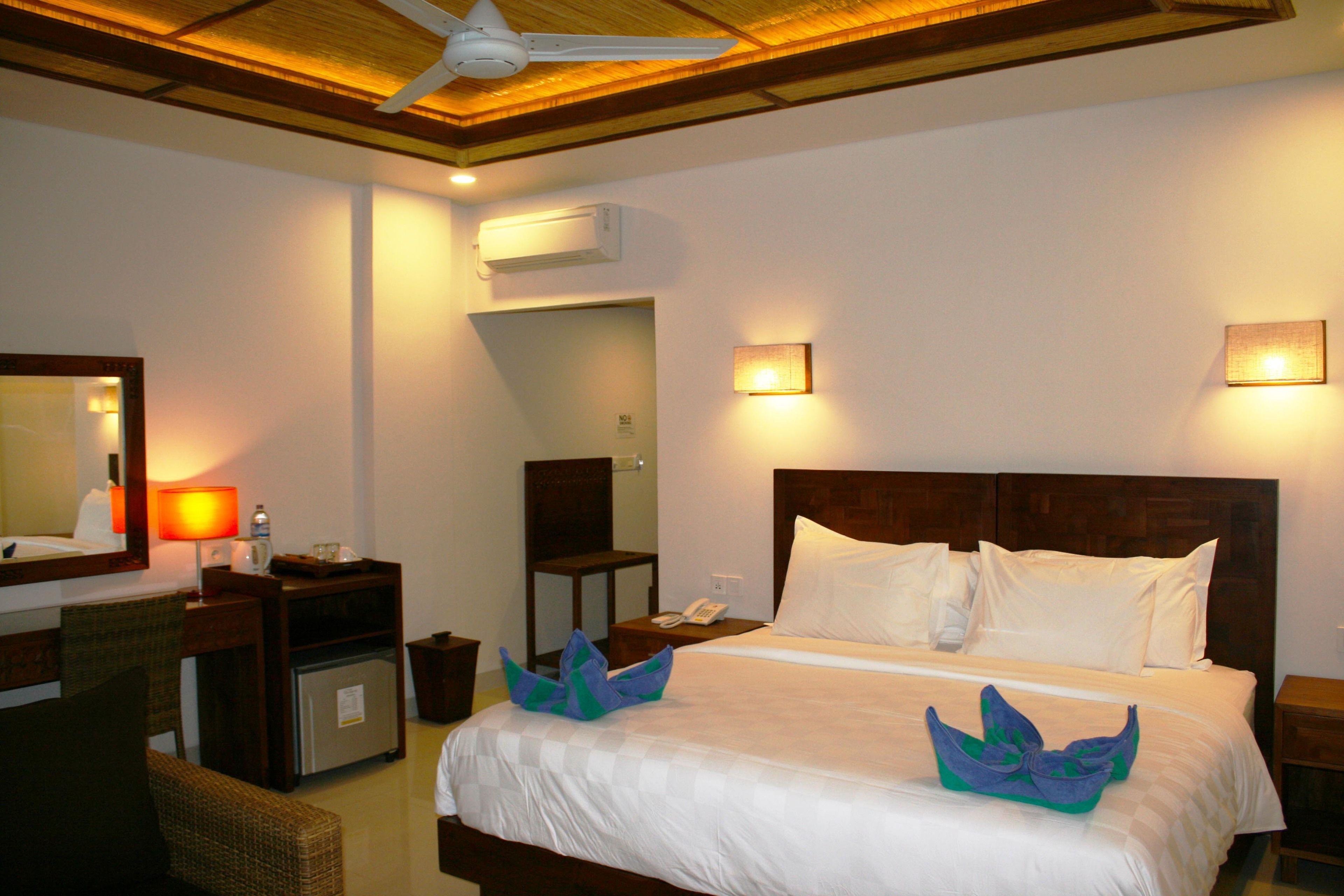 Ein Hotelzimmer mit einem Bett, einem Schreibtisch, einem Sessel und einem Deckenventilator.
