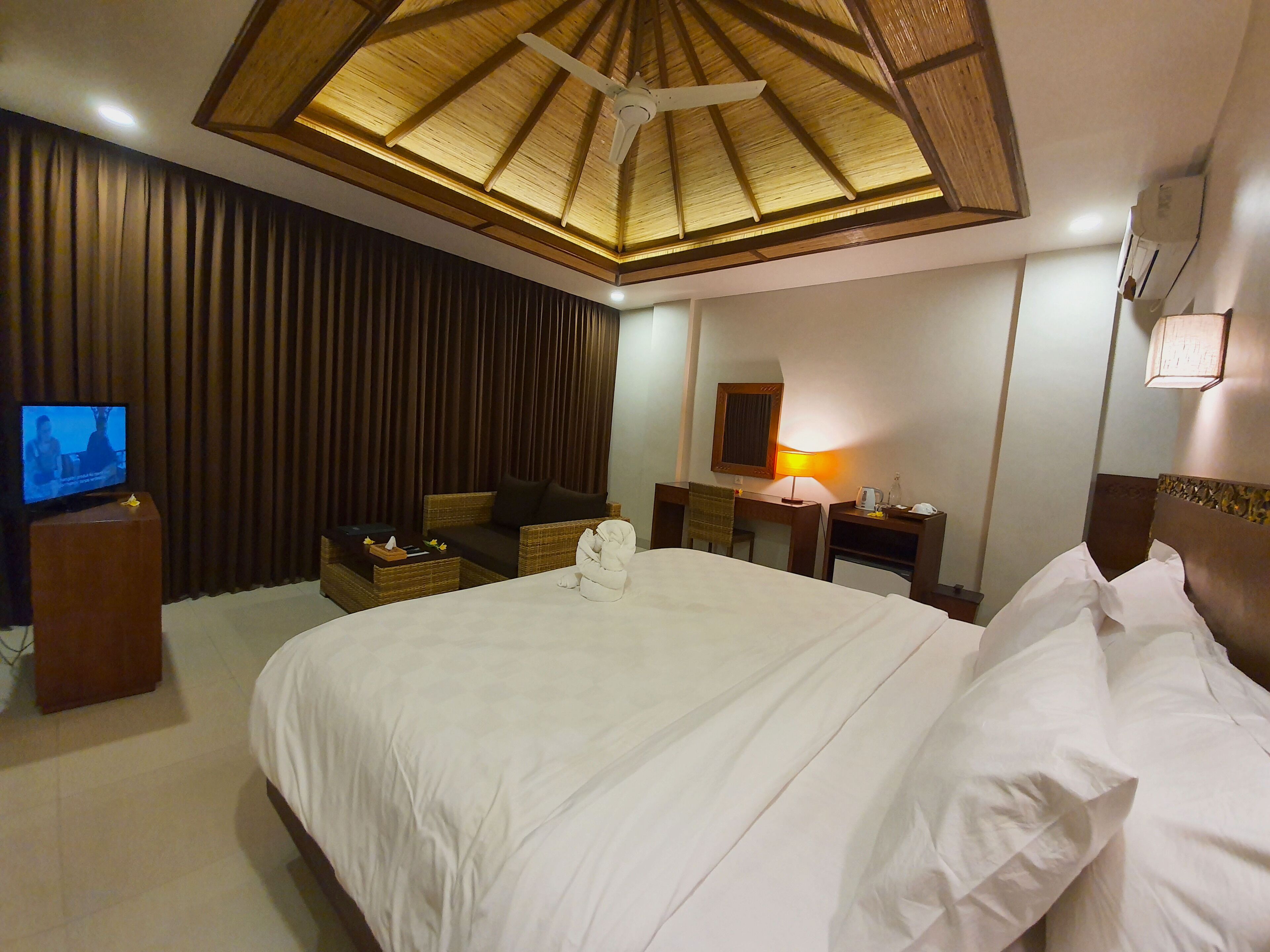A hotel room with a bed, a desk, a chair, a television, and a ceiling fan.