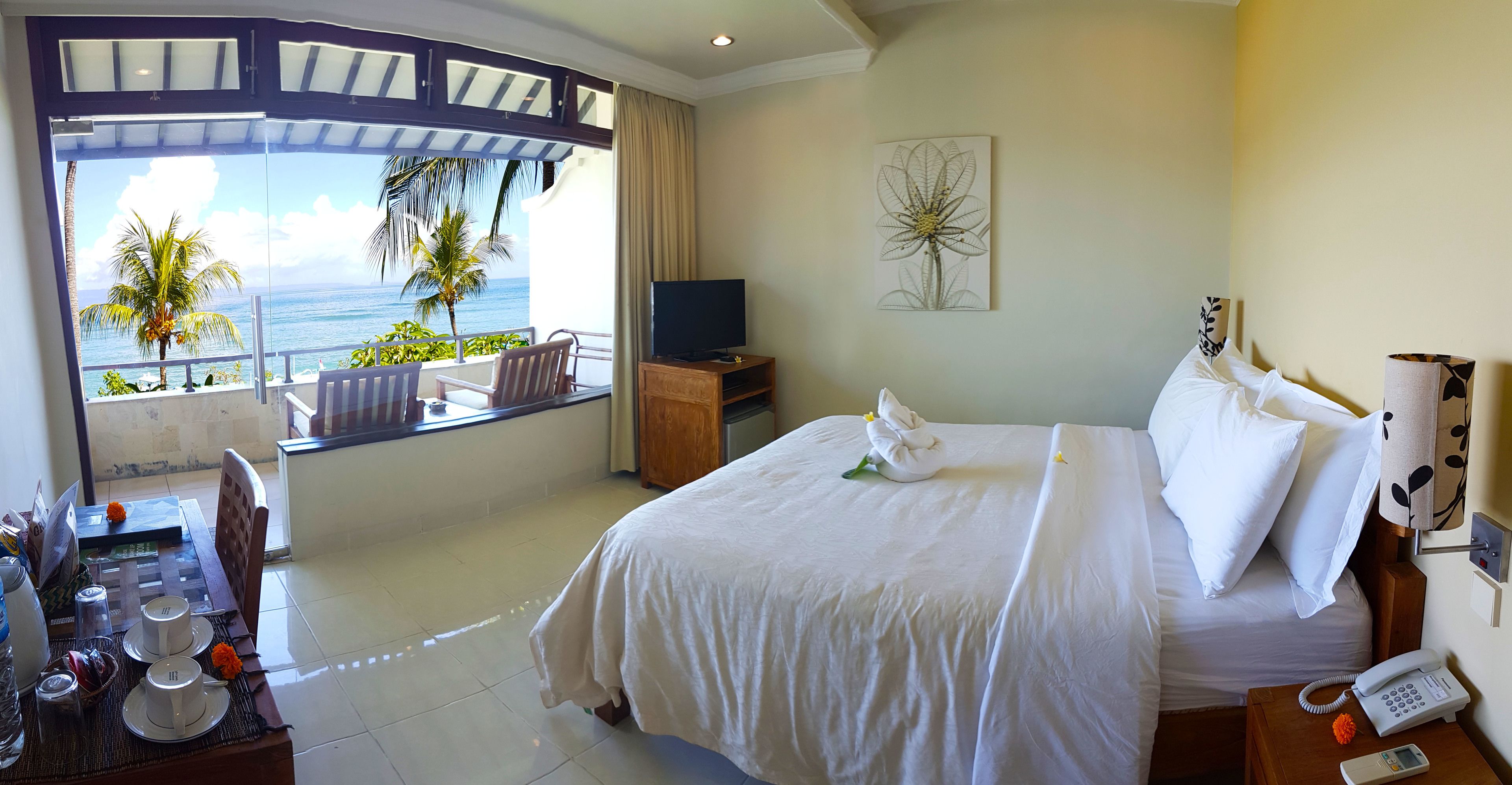 A hotel room with a bed, a TV, a phone, and a balcony with a view of the ocean.