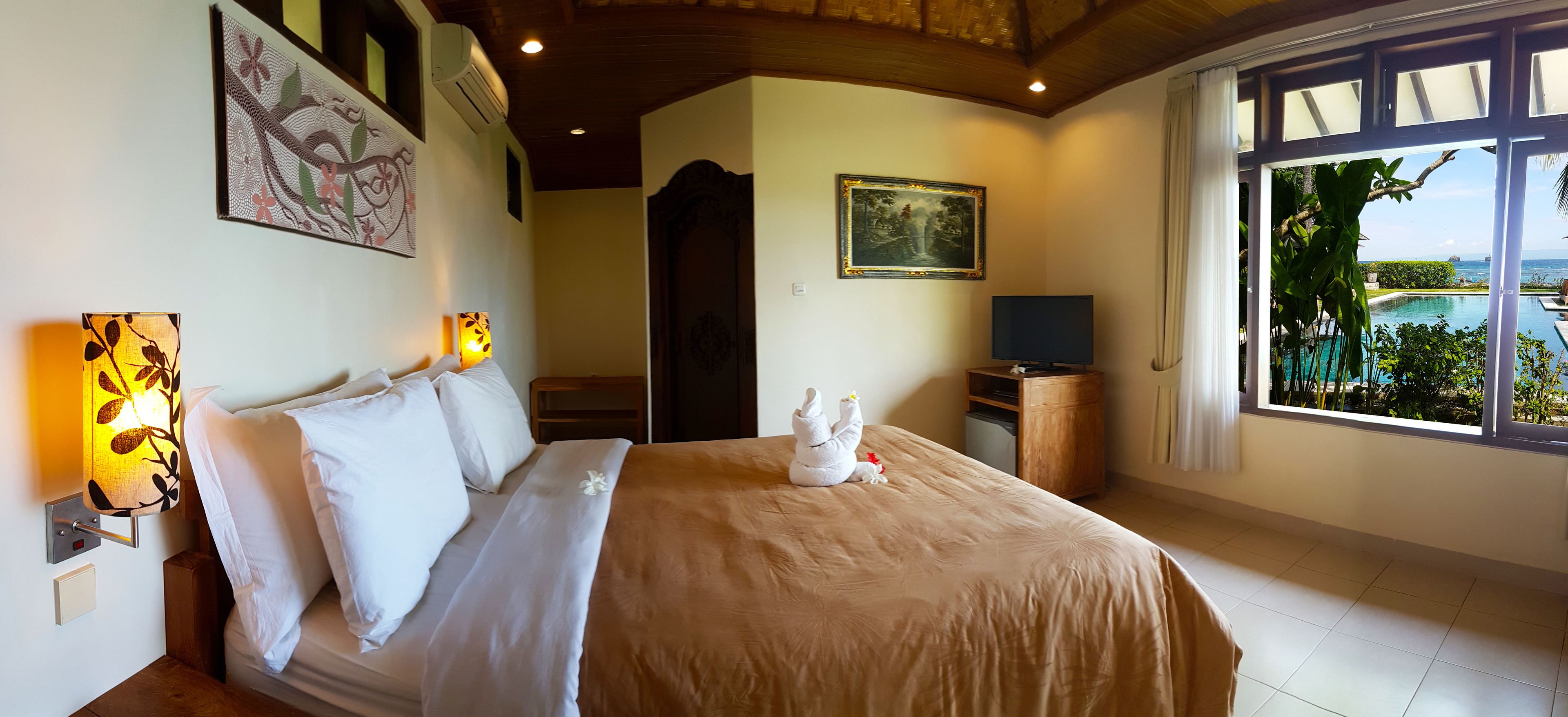 A hotel room with a bed, a TV, a painting, and a view of a pool.