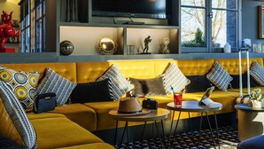 Een moderne woonkamer met een gele bank, gestreepte kussens, een flatscreen-televisie en een raam met uitzicht op bomen.