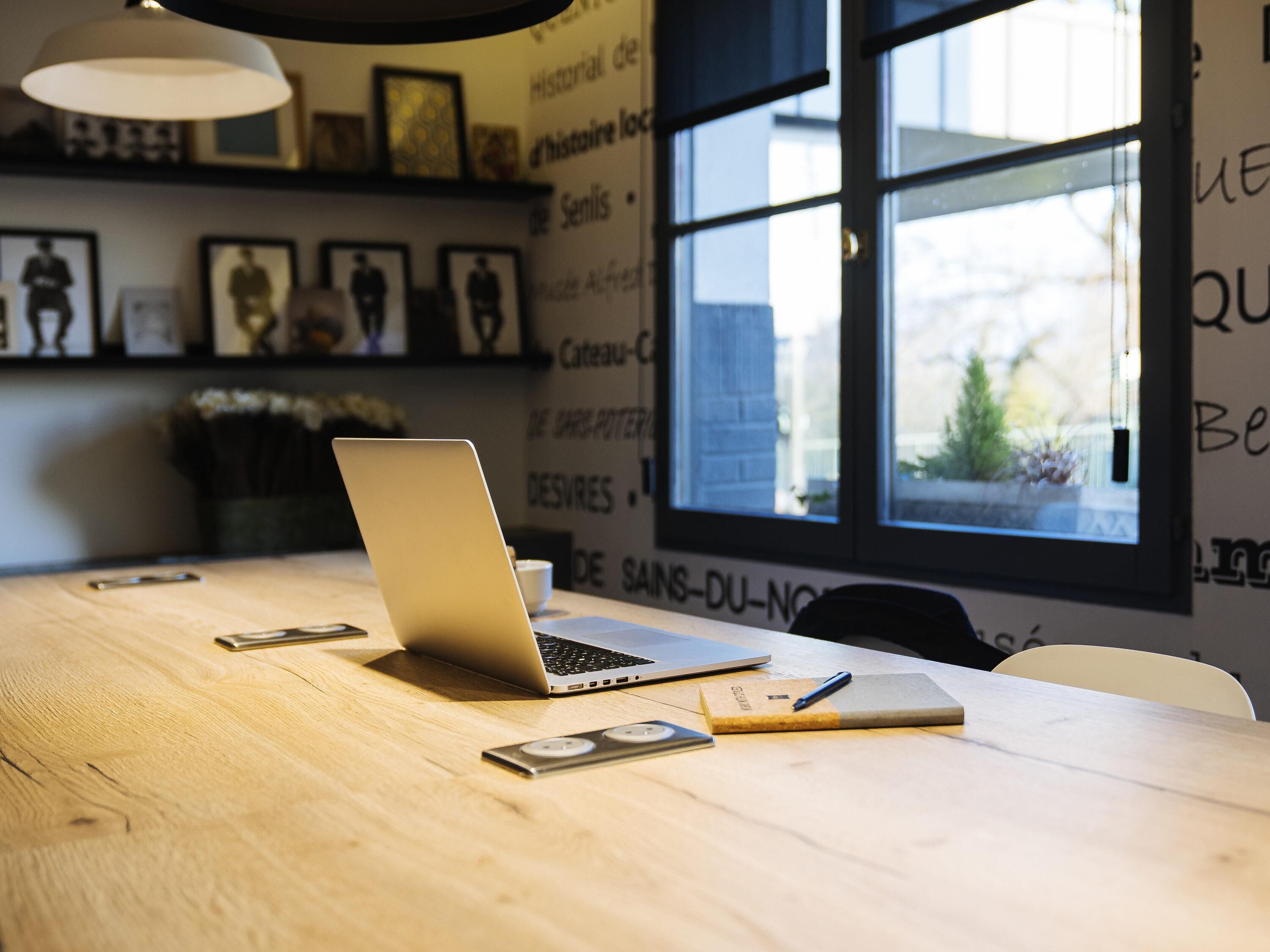 A wooden table with a laptop, a smartphone, a notebook, and a pen.
