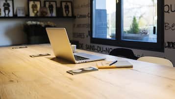 A wooden table with a laptop, a smartphone, a notebook, and a pen.