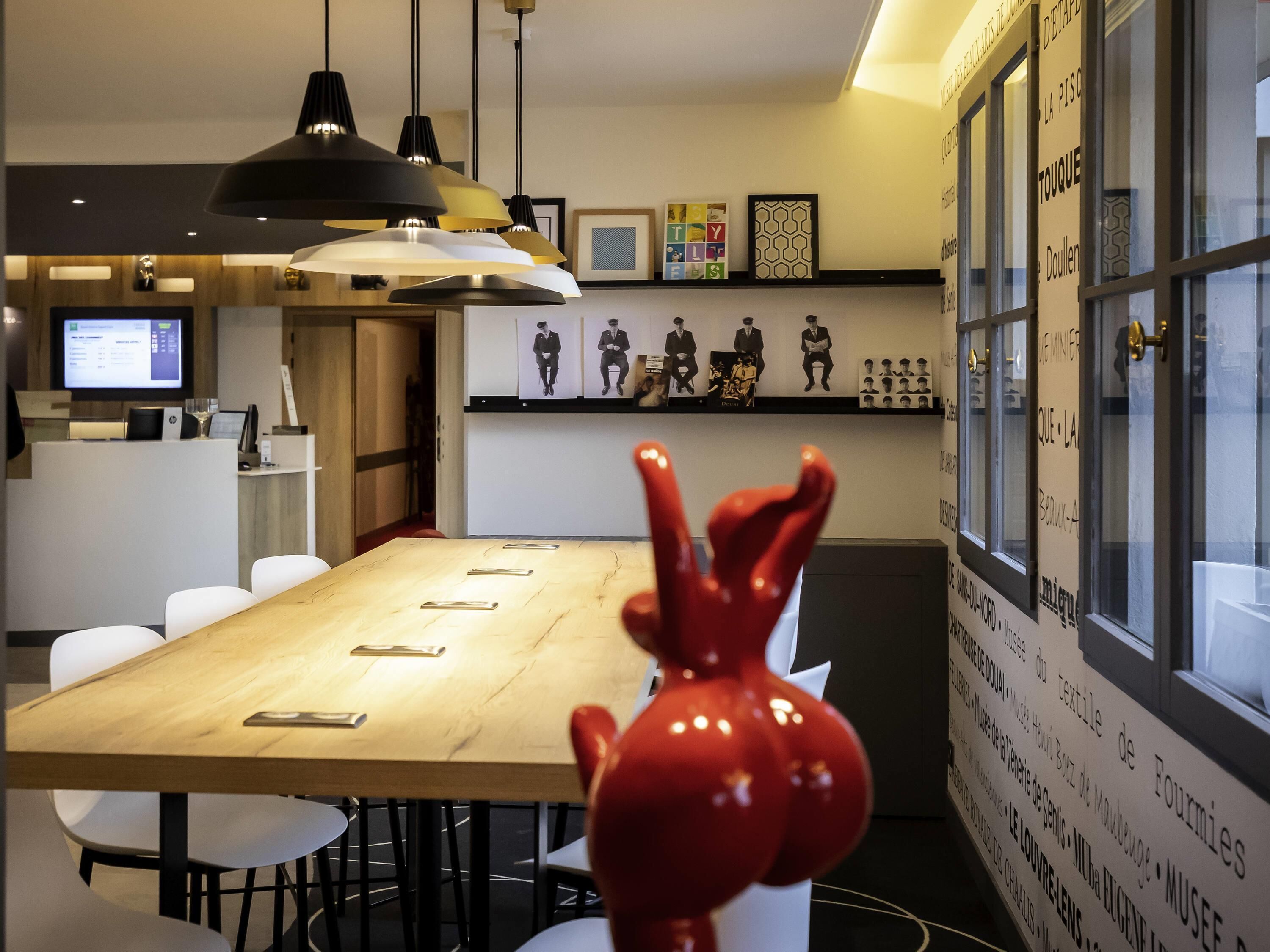 A conference room with a long table, white chairs, pendant lighting, and a red sculpture.