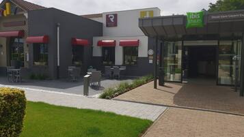 Entrada de hotel con diseño moderno, zona de estar al aire libre y un cartel visible de 'ibis Styles Hotels'.