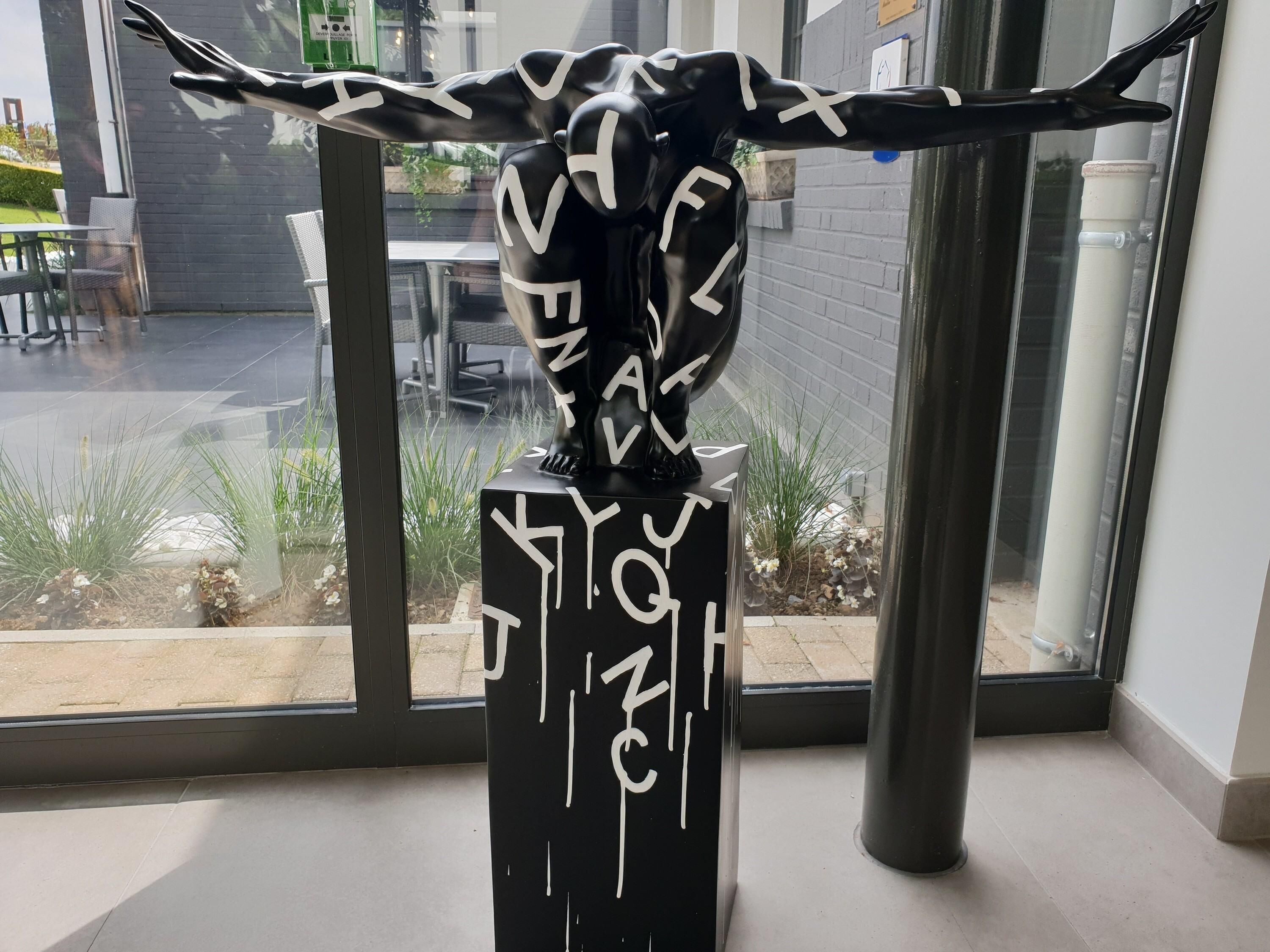 A sculpture of a bull with white markings on a black pedestal, placed indoors near a window.