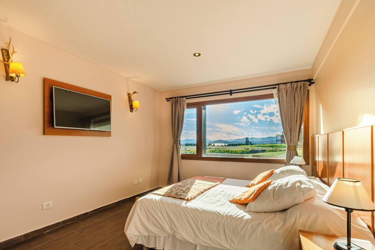 Ein Hotelzimmer mit Bett, Fenster mit Blick, Spiegel und Wandleuchten.