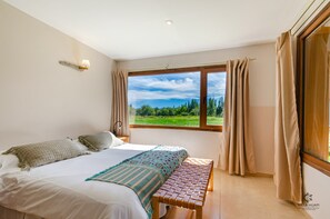 Een slaapkamer met een bed, een raam met gordijnen, een bedlampje en uitzicht op groen.