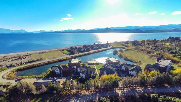 An aerial view of a residential area with houses, a lake, and mountains in the background. - Villa Huapi (Dina Huapi)