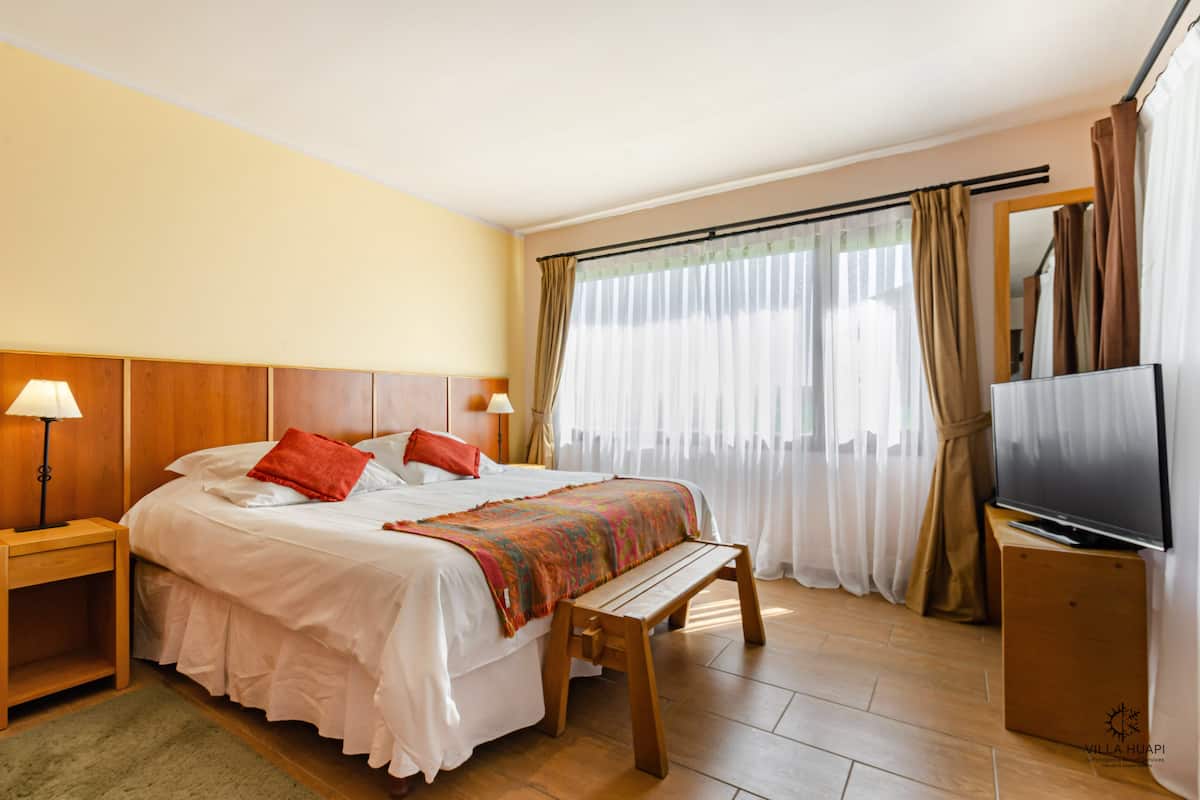 A hotel room with a bed, a TV, a bench, and curtains.
