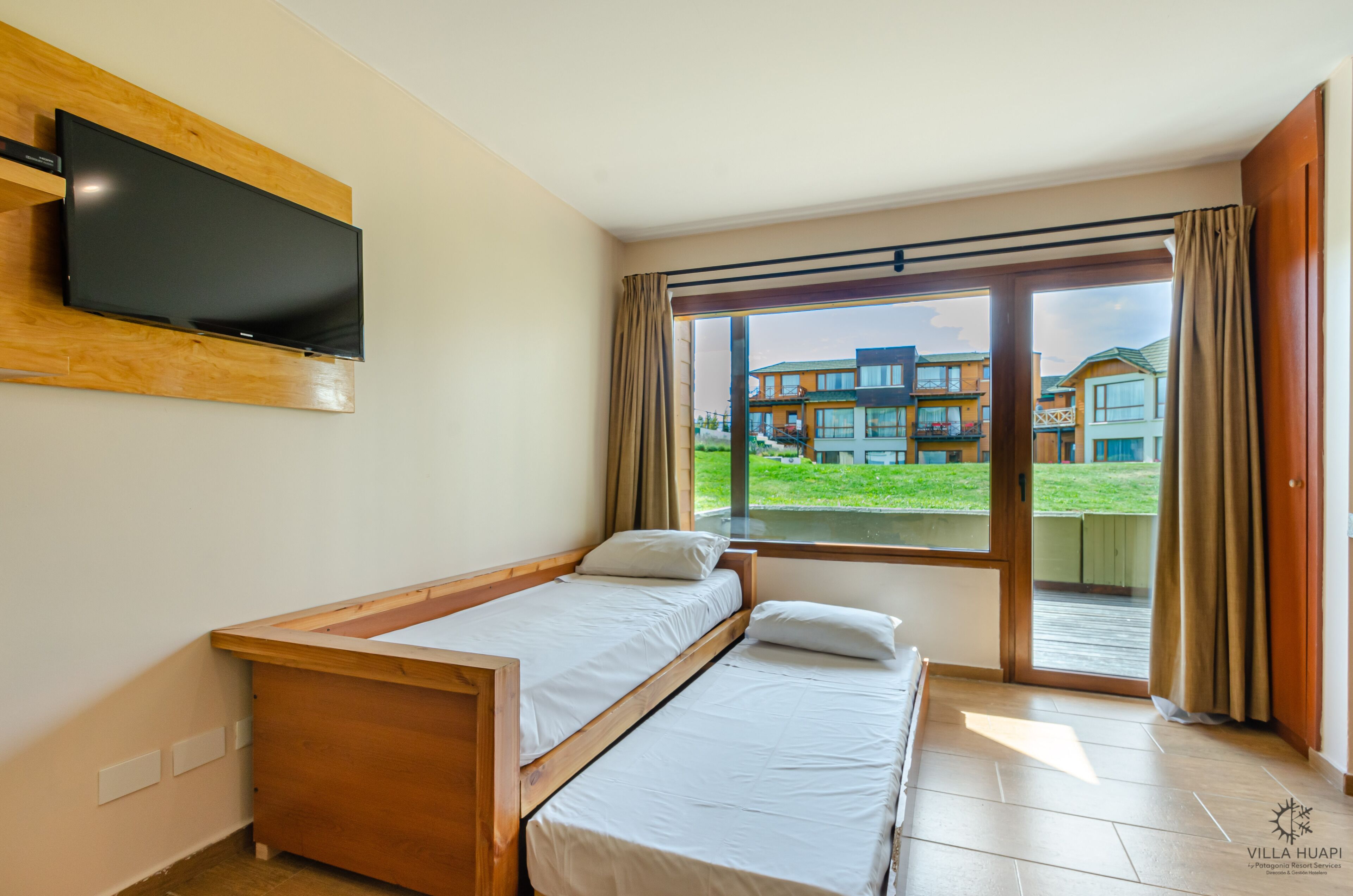 A bedroom with a bed, a TV mounted on the wall, and a window with a view of buildings.
