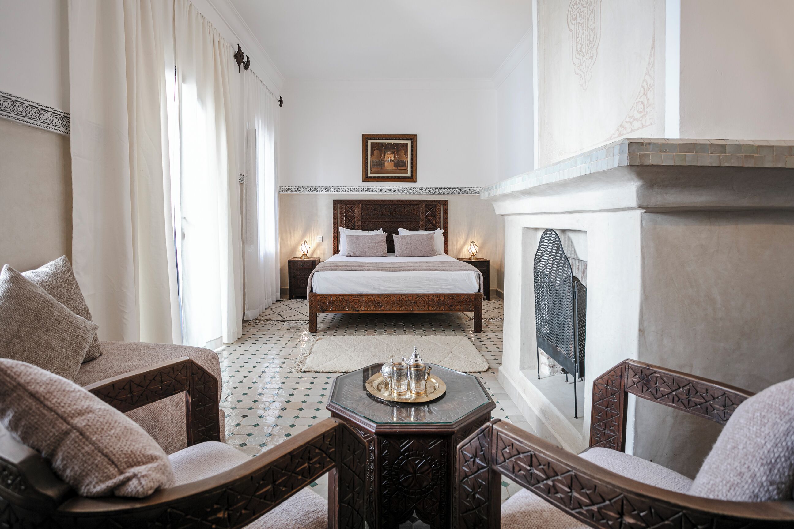 Une chambre d’hôtel comprenant un lit, deux tables de chevet, une cheminée et un coin salon avec des fauteuils.