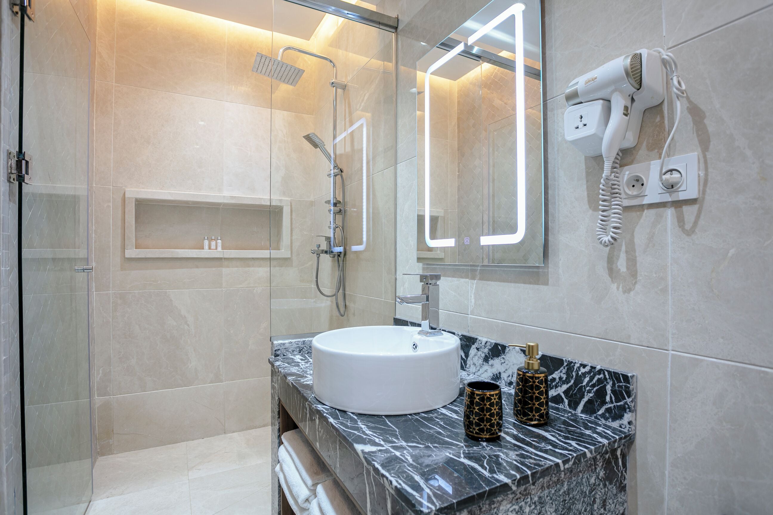 A modern bathroom with a glass-enclosed shower, a white sink, and a hairdryer mounted on the wall.