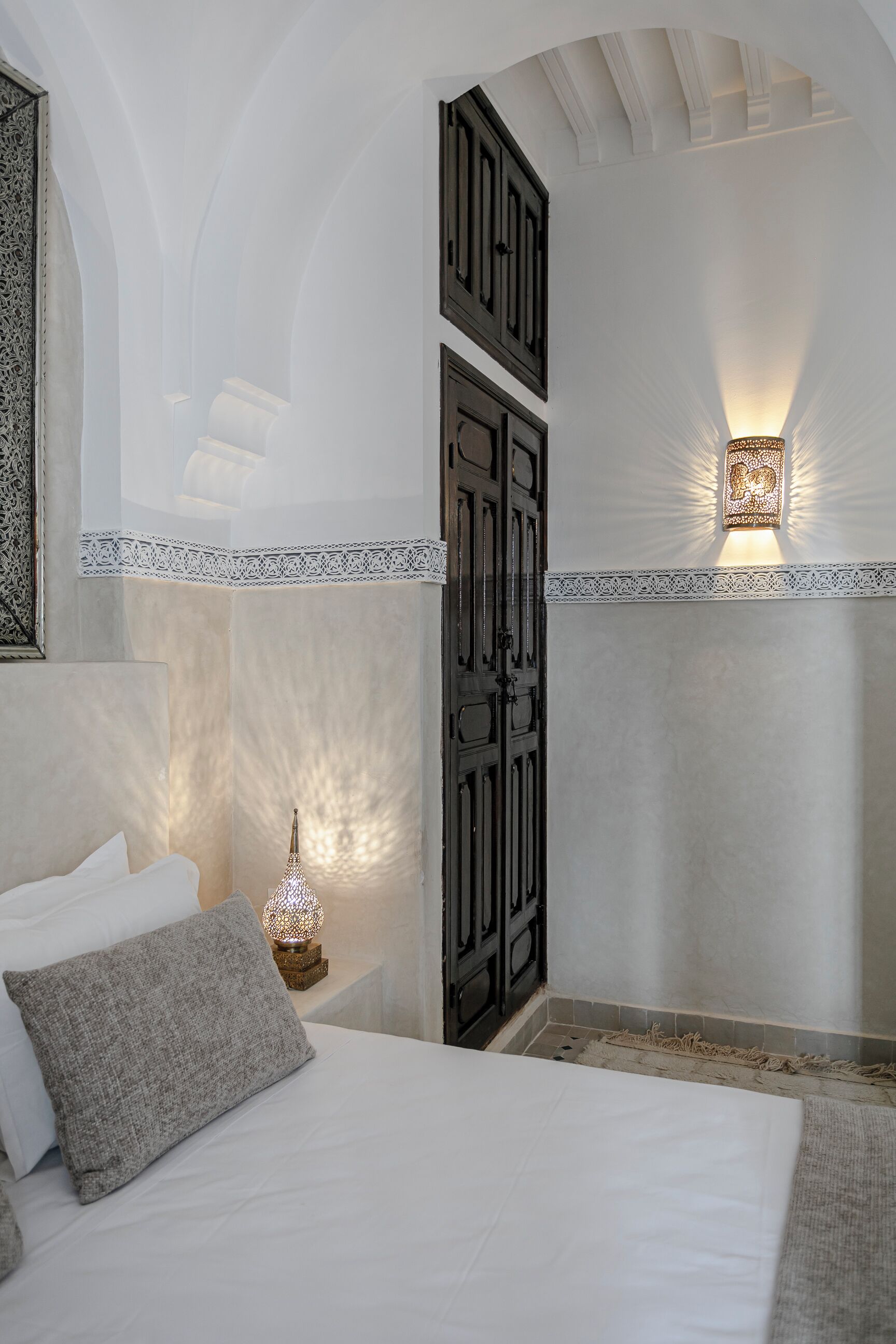Une chambre à coucher comprenant un lit, des oreillers, une table de chevet avec une lampe, des panneaux décoratifs sur les murs et un luminaire au plafond.