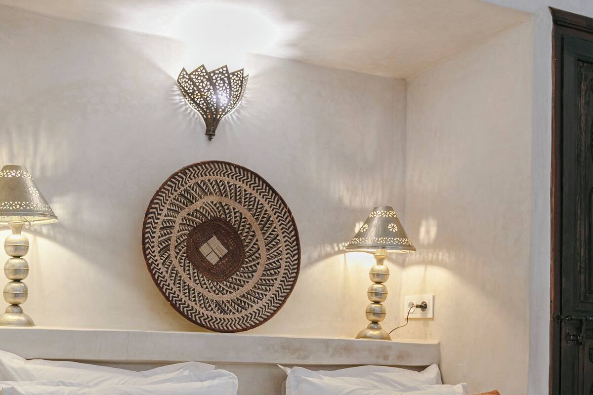 A neatly made bed with white and brown pillows, a decorative wall hanging, and two wall-mounted lamps.