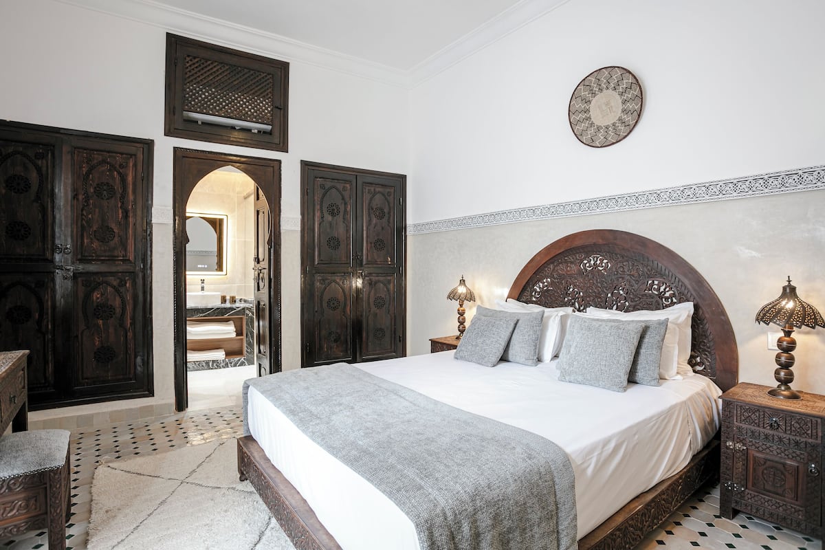 A bedroom with a large bed, dark wooden wardrobe, and a small bedside table with a lamp.