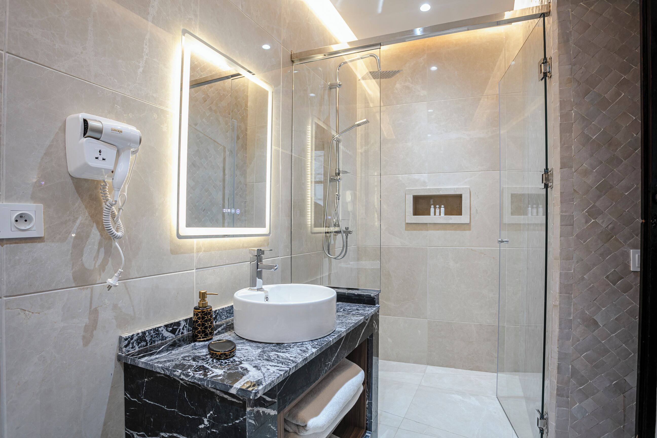 A modern bathroom with a glass-enclosed shower, a built-in sink, and a hairdryer mounted on the wall.