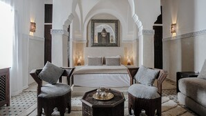 Une pièce spacieuse comprenant un grand lit, deux fauteuils, une table basse et un miroir décoratif.