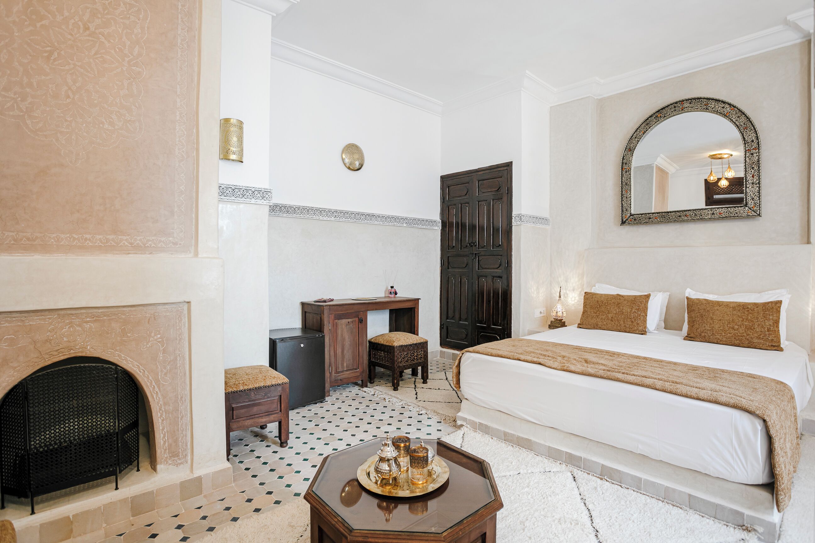 A bedroom with a large bed, a fireplace, a desk, and a mirror.