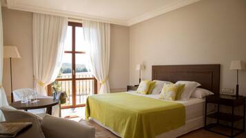Una habitación de hotel con cama, una silla, una mesa y un ventanal con cortinas.
