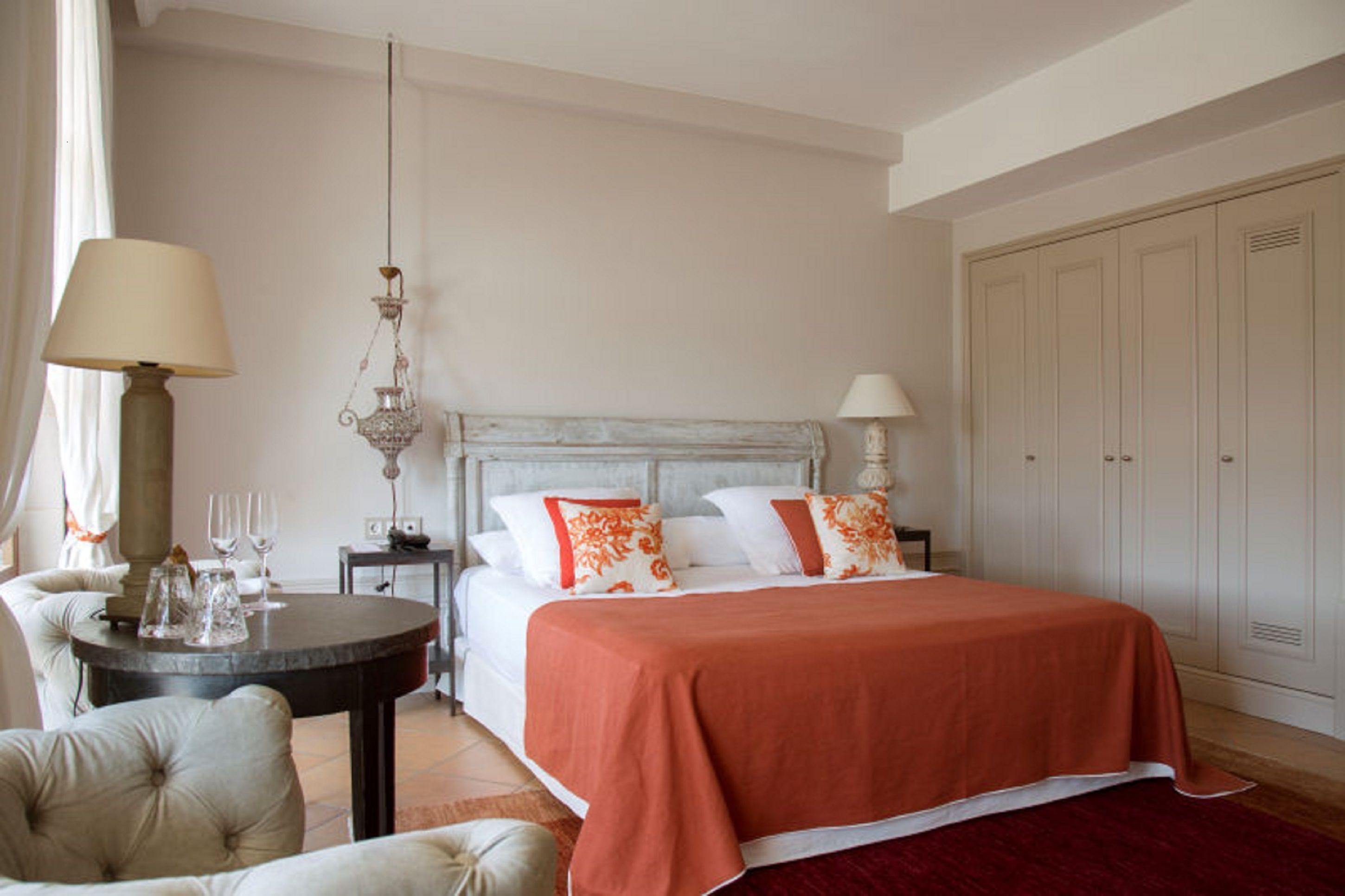 Une chambre à coucher comprenant un lit, des tables de chevet, un lustre, une armoire et une table ronde avec une lampe.