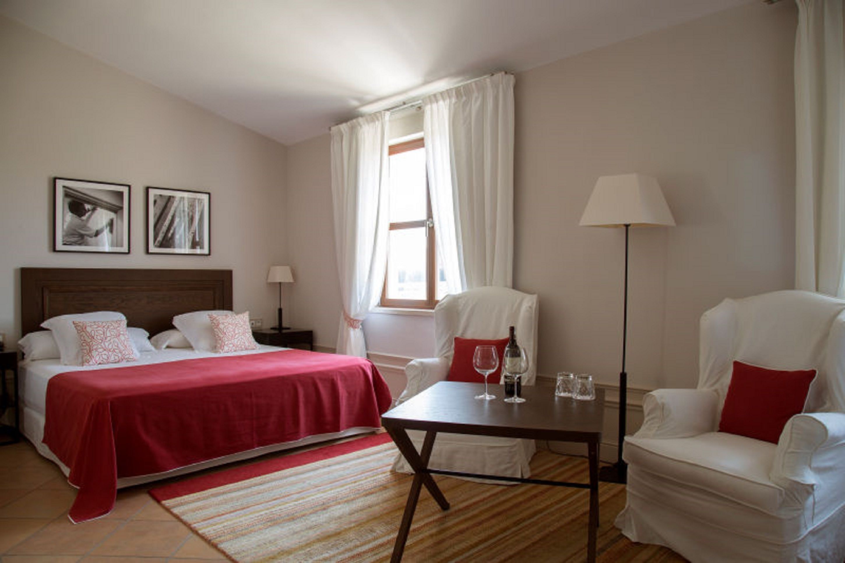A hotel room with a bed, a chair, a table, and a lamp.