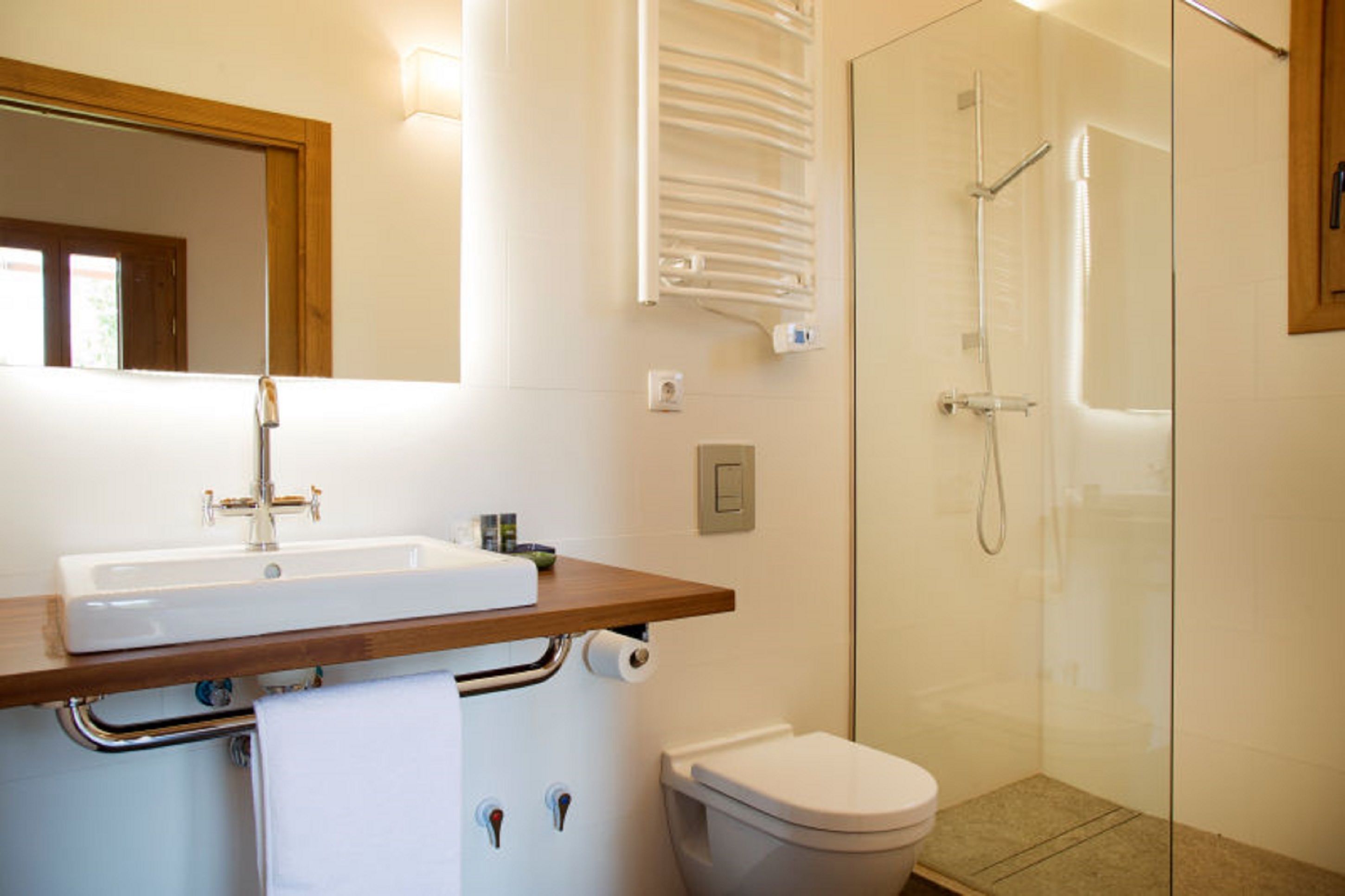 Un baño con lavamanos, espejo, toallero, inodoro y zona de ducha con mampara de cristal.