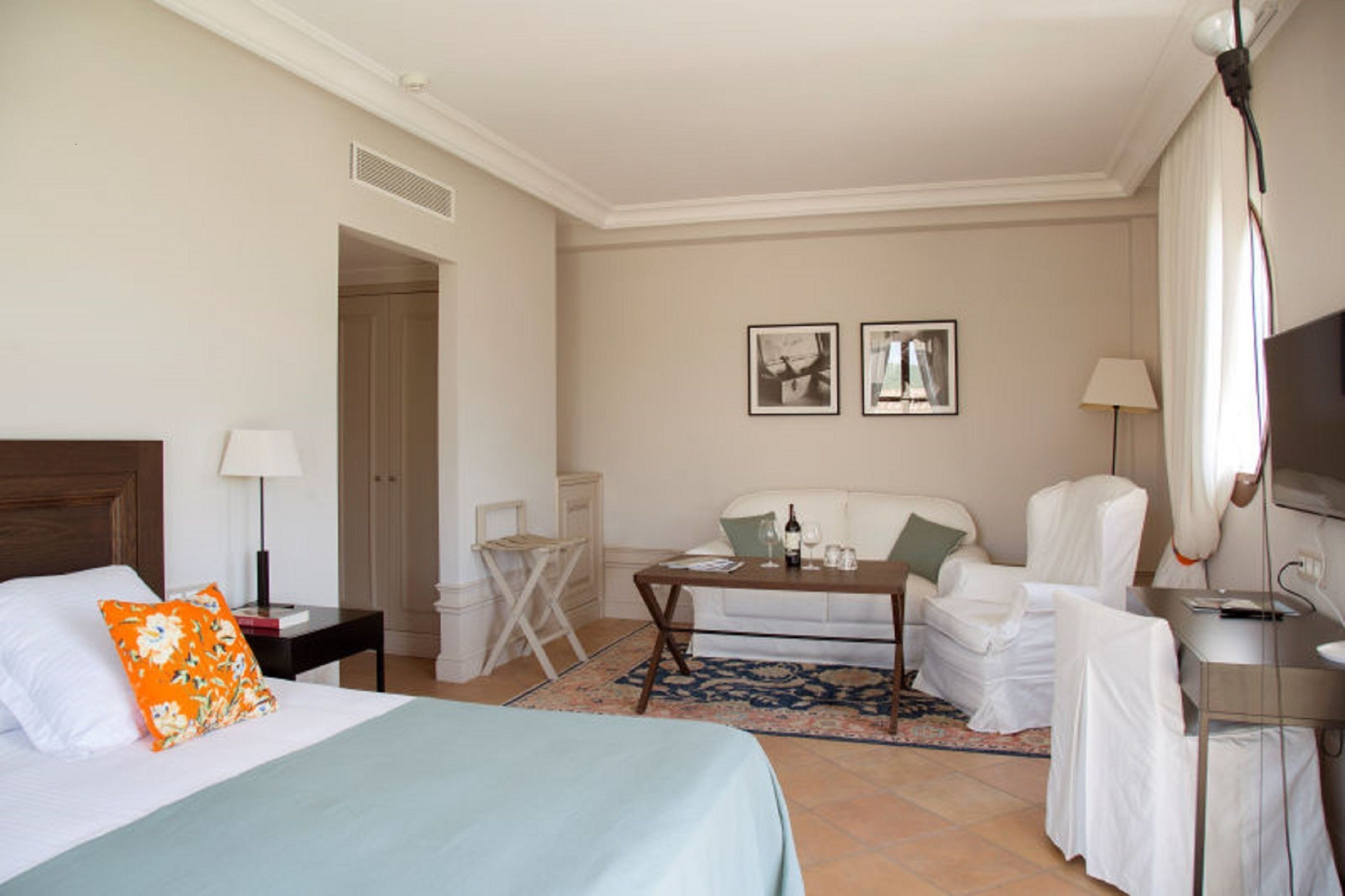 Une chambre d’hôtel comprenant un lit, un bureau, une chaise, un canapé et deux tableaux encadrés accrochés au mur.