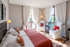 Habitación de hotel con una cama grande, dos sillas, una mesita y vistas al exterior.