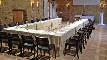 A conference room with a long table set for meetings, stone walls, and a projector screen.