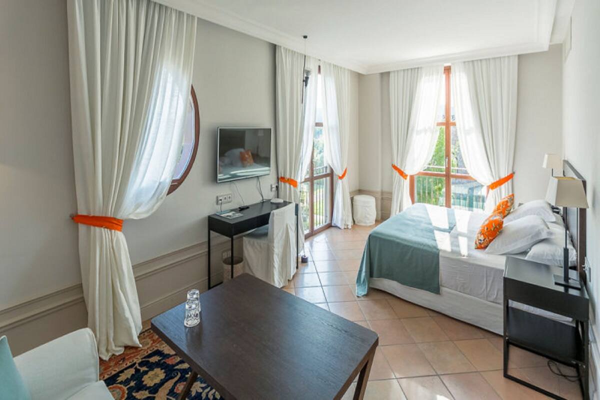A hotel room with a bed, a desk, a TV, and a window with curtains.